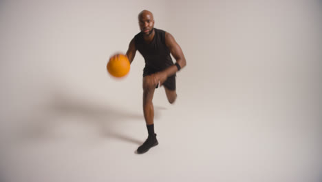 Studioaufnahme-In-Voller-Länge-Eines-Männlichen-Basketballspielers,-Der-Den-Ball-Vor-Weißem-Hintergrund-Dribbelt-Und-Hüpft-3